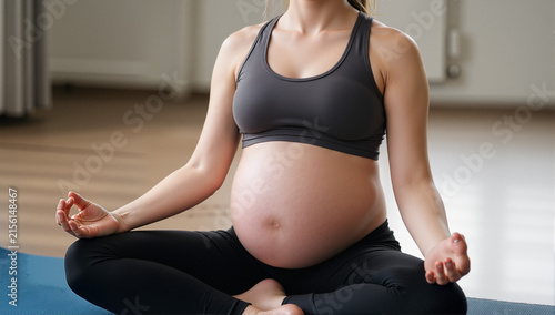 Close-up of young pregnant woman sitting on exercise mat and meditating during her training
