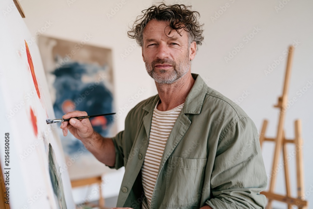 Fototapeta premium Middle-aged male artist portrait painting on canvas in bright studio for workshop background and creative banner design