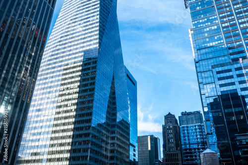 Modern glass skyscrapers rise against a clear blue sky, featuring reflective facades, geometric architecture, corporate offices, and a dynamic urban business district in a contemporary city.