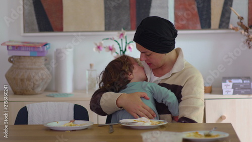 Bild auf Leinwand Mother comforting crying toddler at dining table in family home during cancer re