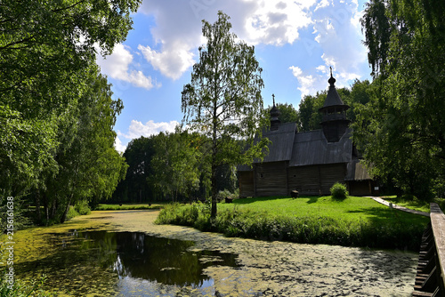An old wooden church near a small river surrounded by forest.