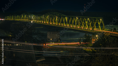 Foto Illuminated steel truss bridge over the Danube River at night, surrounded by urban lights and long-exposure vehicle light trails