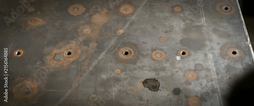 Close-up of a heavy industrial welding table with rusted spots and drilled threaded holes in a workshop setting