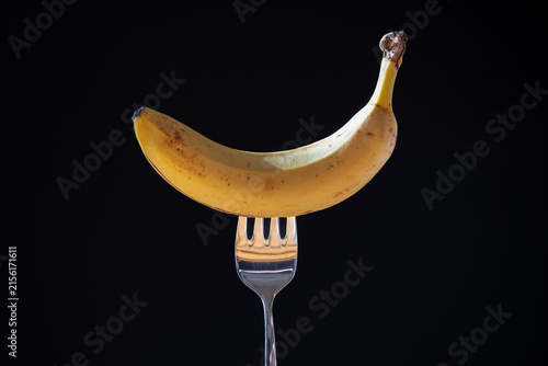Yellow ripe banana balanced horizontally on metal fork against black background