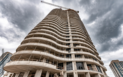 Tall tower crane above a huge skyscraper under construction against a stormy sky