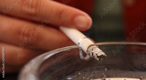 Foto Woman flicking ash from cigarette into ashtray outdoors, closeup