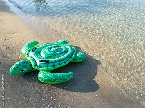 Inflatable green turtle float resting on sandy beach near clear water shoreline