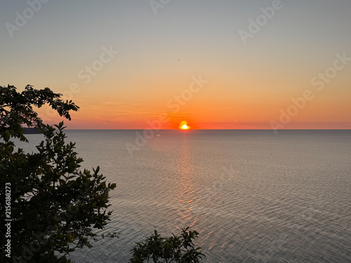 Sunset over calm lake with silhouetted trees along the shoreline and vibrant orange sky