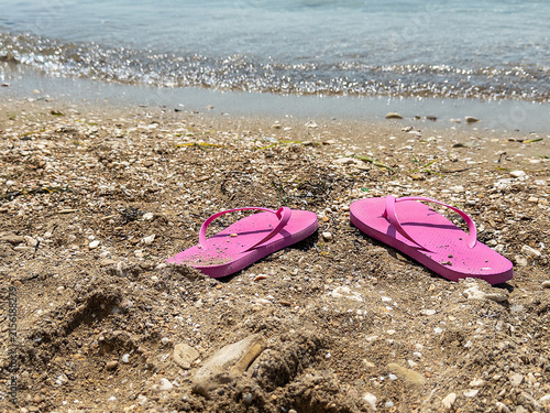 Pink flip-flops resting on sandy beach shore with gentle waves in the background
