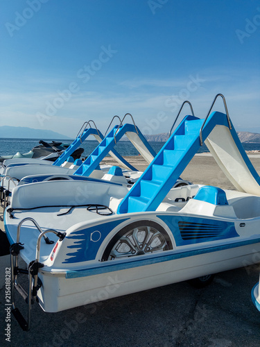 Pedal boats lined up on sandy beach with blue sky and ocean in background