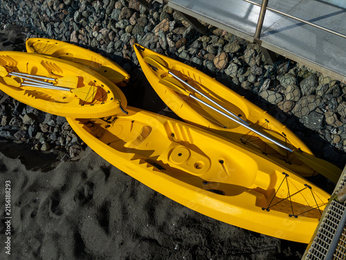 Yellow kayaks arranged on rocky shore beside wooden dock in bright sunlight