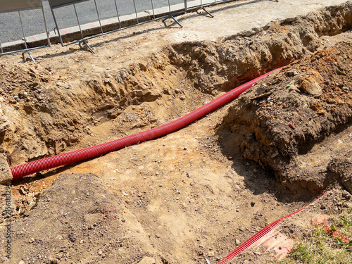 Excavation site with red drainage pipe installed in trench on construction area near road