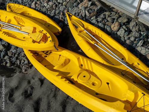 Yellow kayaks stacked on rocky beach with sunlight illuminating their vibrant colors