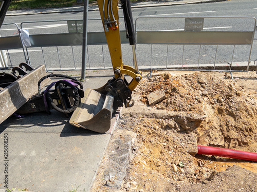 Excavator bucket digging into ground at construction site with safety barriers and tools nearby