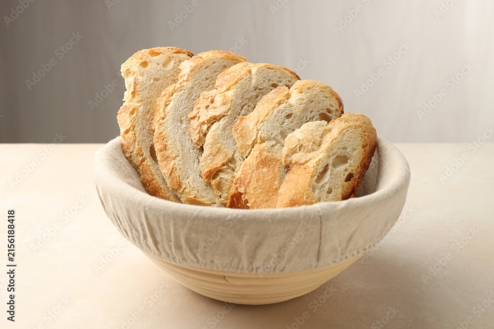 Obraz premium Fresh bread slices in basket on beige table, closeup