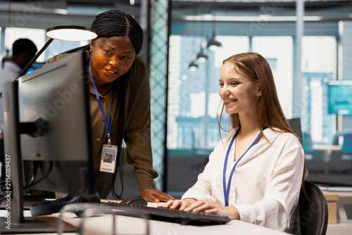 Friendly IT team leader teaches a young software developer to use artificial intelligence, guiding the junior employee through AI tool integration and deep learning APIs during office training.