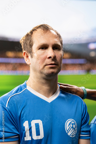 фотографія Soccer player in a blue jersey listens to the national anthem shoulder to shoulder with teammates at the pre-match opening ceremony, showing team spirit inside the stadium ahead of kickoff