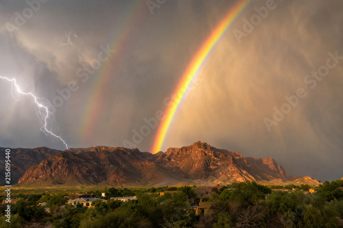 Dramatic rainbow and lightning over the Superstition Mountains near Mesa, Arizona during a summer monsoon storm, with rain-filled skies and rugged desert landscape creating a striking Southwest weathe