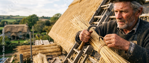 Man working as a thatcher bundles straw for a roof repair. Skilled artisan tying reeds with a metal hook to restore a traditional cottage. Heritage craft and manual labor technique.