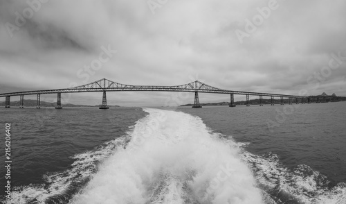 Konstfotografi Black and white view of Richmond-San Rafael Bridge behind boat wake