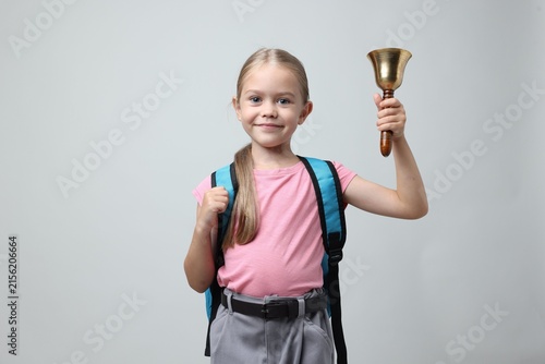Little girl ringing school bell on light grey background