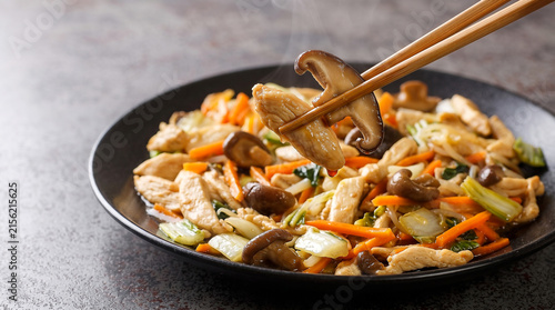 Enjoy a vibrant chicken and mushroom stir fry dish for chop suey day, featuring fresh vegetables and steam while being lifted by wooden chopsticks high quality