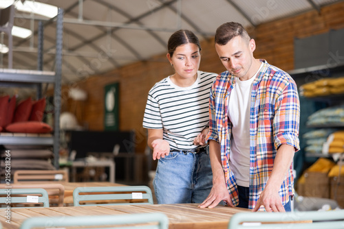 Canvas Print Girl with male friend buyers before buying furniture inspects table goods for defects and flaws