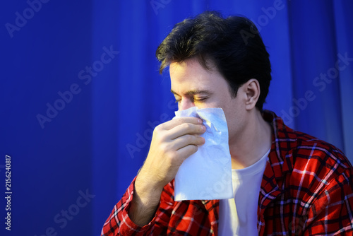 Fotografie Sick man with flu symptoms uses a tissue for sneezing