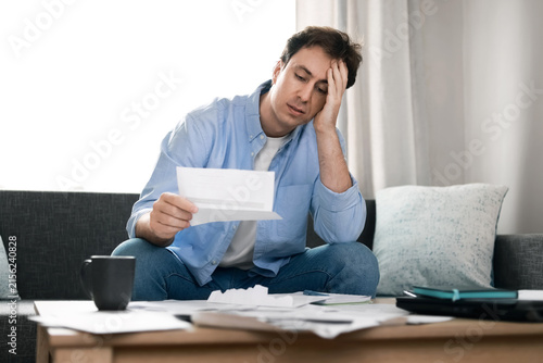 Quadro su tela Stressed man reads overdue utility bills at home