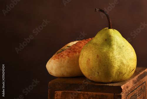 Pear Still Life. An Anjou Pear and a bread roll on a rustic wooden box with a mottled brown background.
