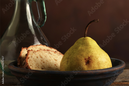 Pear and Bread Still Life. An Anjou Pear and slices of bread bread on a rustic wooden table with a mottled brown background.
