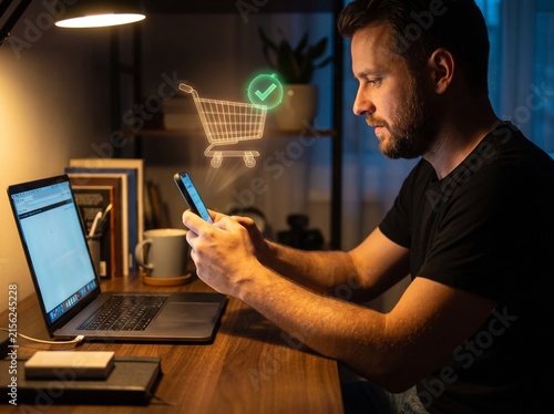 Young man shopping online with smartphone at home office desk in evening