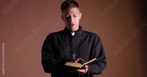 Priest in cassock reading Holy Bible on beige background