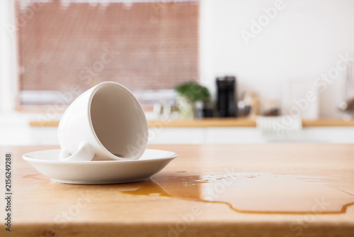 Obraz na plátne Spilled coffee from an overturned white ceramic cup and saucer on a light wooden