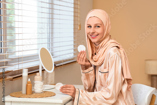 Quadro su tela Smiling young muslim woman in hijab and pajamas holding cotton pads for skincare