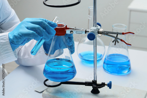 Quadro su tela Scientist in blue gloves pouring blue liquid from a test tube into an erlenmeyer