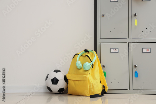 Yellow backpack with mint green headphones and a soccer ball next to school l...