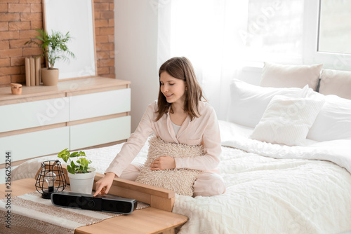Young happy woman turning on wireless portable speaker at home