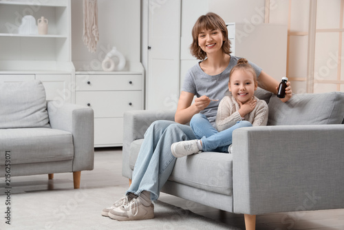 Ill little girl and her mother with cough syrup sitting on sofa at home