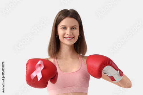 Young woman in boxing gloves with pink ribbon on white background. Breast can...