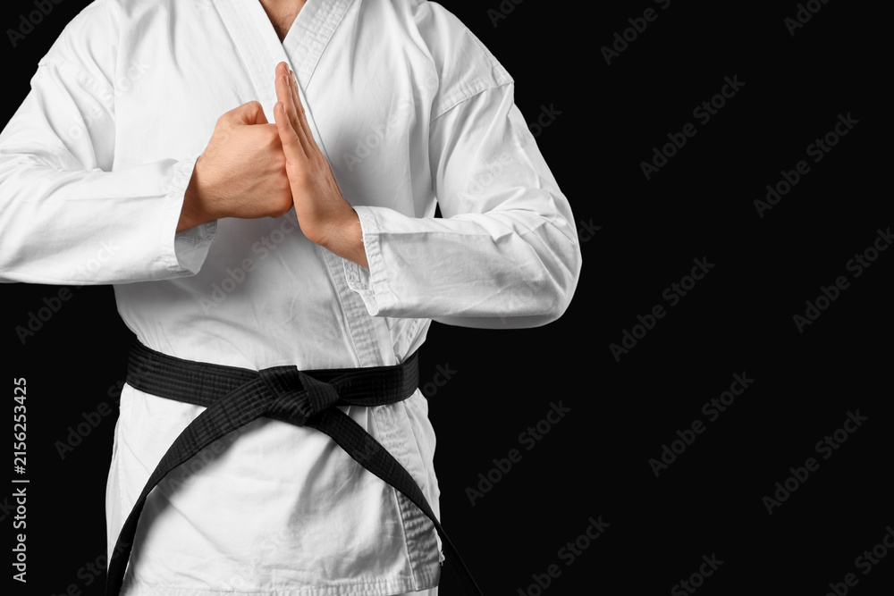 Fototapeta premium Young man practicing karate on black background