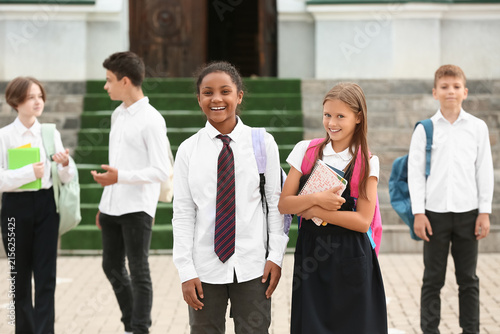 Group of happy pupils with stationery near school outdoors