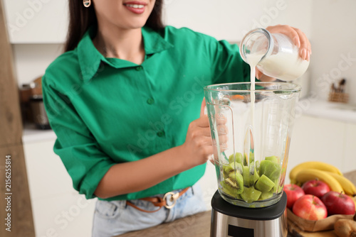 Young woman pouring milk into blender in kitchen, closeup