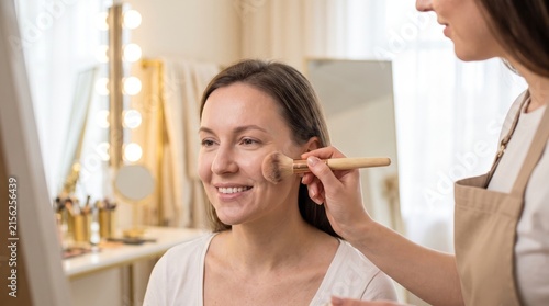 Professional makeup artist applying cosmetics to a woman with a brush in a brightly lit studio.