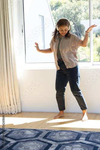Fotografie African American woman moving near large window on wood floor wearing over-ear w