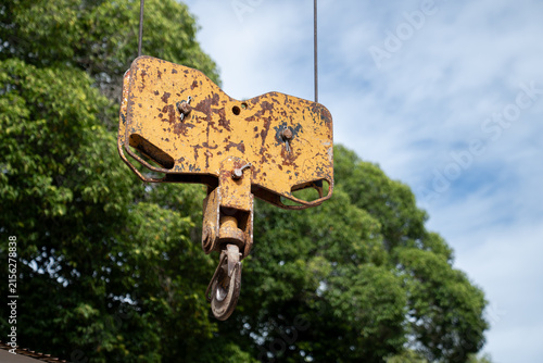 Canvastavla An old yellow crane sheave block with a steel hook hangs outdoors