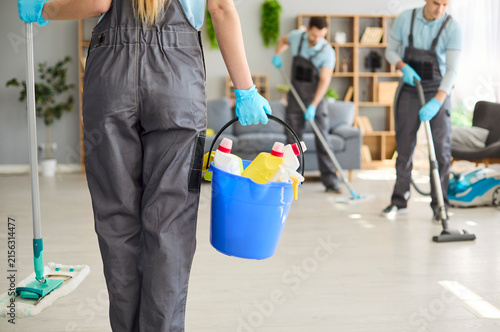 Cleaners team cleaning service with bucket gloves. Uniformed workers sanitize a bright workspace using mop and vacuum carrying supplies for deep cleanup. Shows hygiene and teamwork in service.