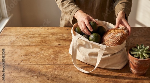 Woman unpacking healthy groceries from reusable tote on wooden table