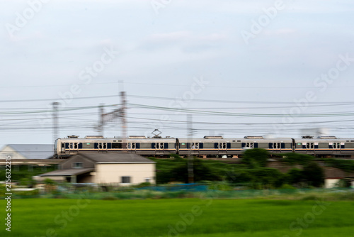 京都府の田園地帯を走るJR旅客列車。緑豊かな水田と鉄道が織りなす、日本の夏の日常風景。