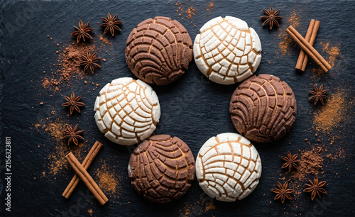 symmetrical vanilla and chocolate conchas forming a circle on a matte black stone surface,  Geometric seashell pattern crust contrast against dark background. 